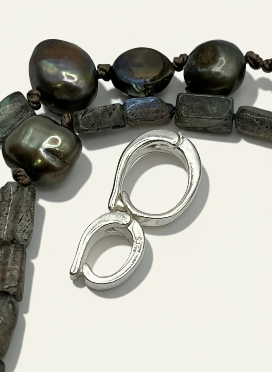 Close-up of a black pearl and labradorite strands with silver pearl enhancers shown for sizes- med and small- on a white background