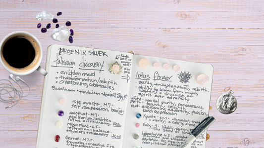 Open artist’s notebook showing symbolic sketches and handwritten notes for a Talisman Discovery Session, surrounded by silver pieces and gemstone references — a glimpse into the creative process of matching story to stone.