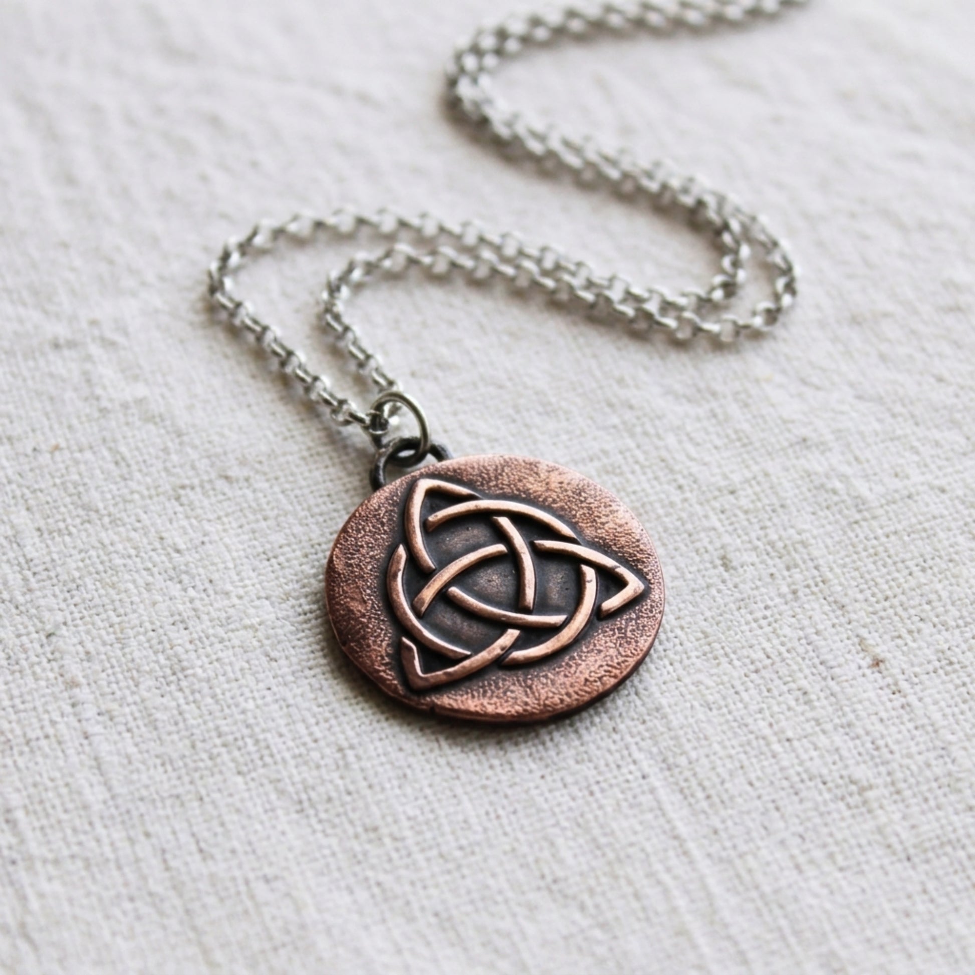 1" Copper Triquetra charm on silver rolo chain with linen background