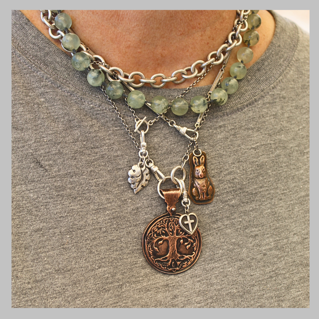 Photo of necklace stack on grey shirt background, included silver chains, silver leaf, copper rabbit, copper tree of life, prehnite anchor strand and various connectors.